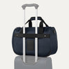 Blue tote with a black rear strap over suitcase handle on a white background