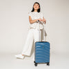 Person standing with the Travelpro Maxlite Air Carry-On Hardside Spinner in Teal, showcasing its compact, stylish design.