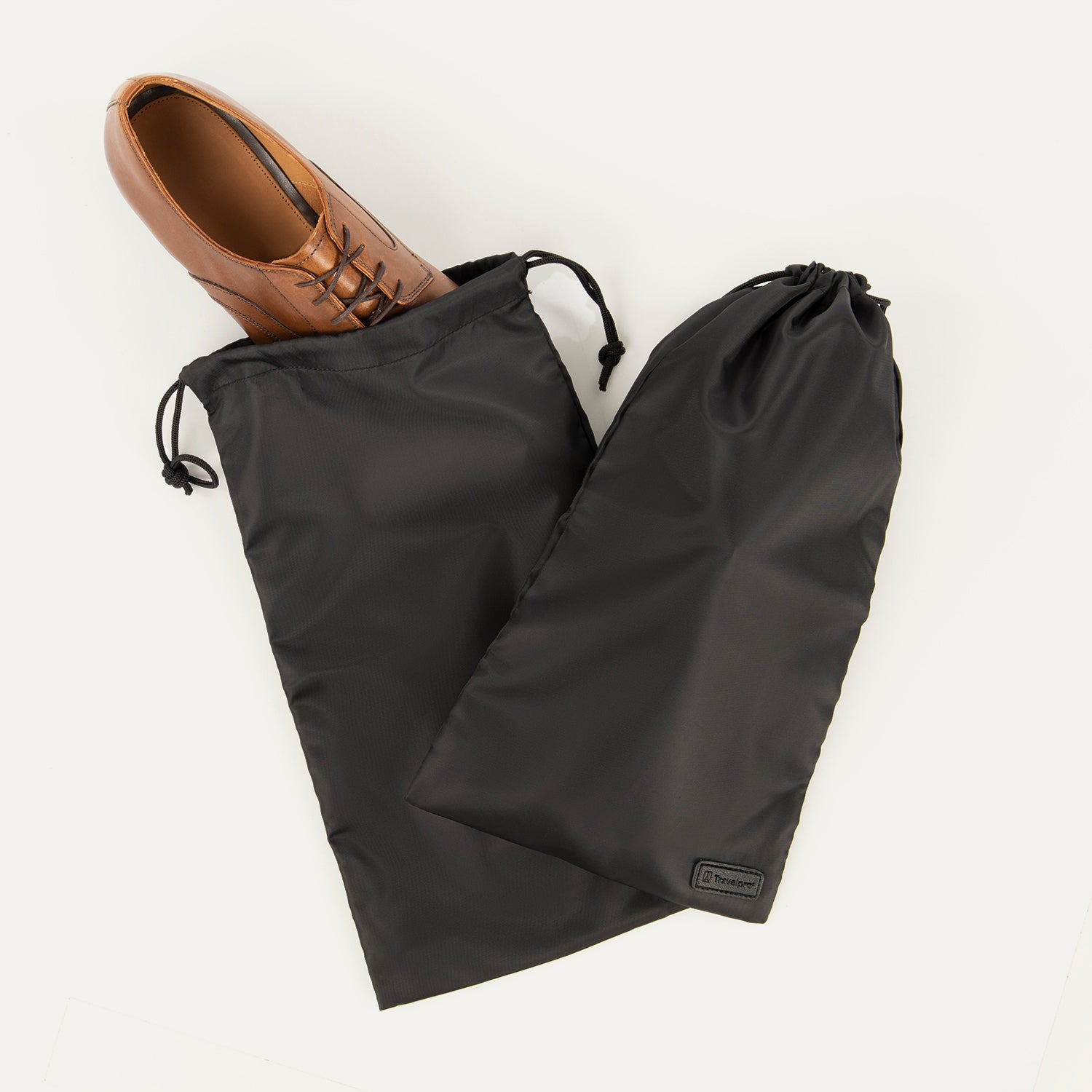 A pair of black Travelpro Essentials shoe bags with a single shoe placed in one of the bags, on a white background.