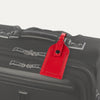 Red leather luggage tag with buckle strap, attached to the handle of a black suitcase.