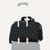 Travelpro® Essentials™ 2-in-1 Travel Tote & Cooler in Black, shown securely attached to a rolling suitcase handle using its rear strap, demonstrating its convenient stacking ability