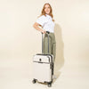 Woman pulling a Travelpro® x Travel + Leisure® Carry-On Spinner in White Sand by its telescoping handle.