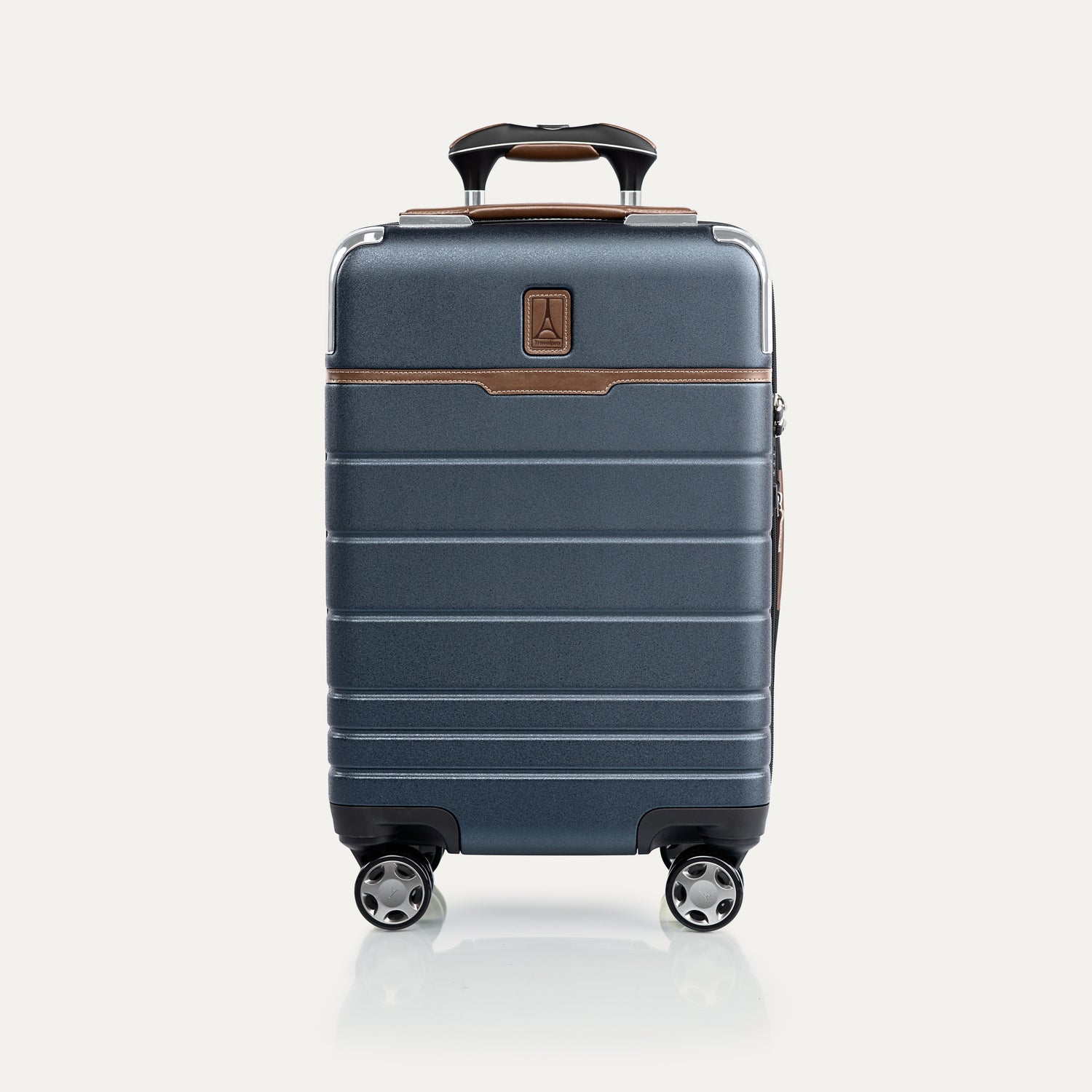 Front view of T+L Compact Carry-On Spinner in Monaco Blue, showing textured finish, tan accents, and grooved paneling.