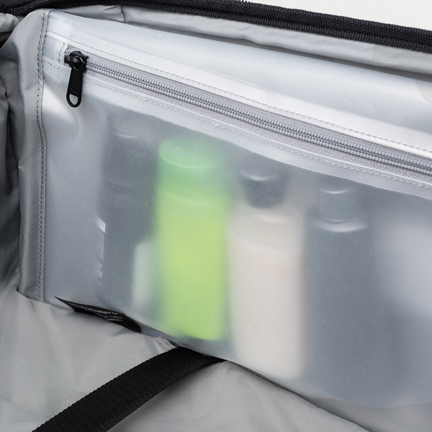 Clear interior view of suitcase with translucent zippered pouch holding upright travel-size toiletry bottles.