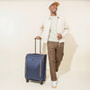 Traveler pulling the Crew™ Classic Medium Check-In Spinner in Patriot Blue, highlighting its durable construction, smooth-rolling spinner wheels, and extended telescopic handle.