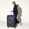 Person walking with the Travelpro Platinum Elite Large Check-In Spinner in Camouflage, holding the extended handle.