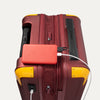 Travelpro x Surgeon Spinner in Daring Red with yellow accents, shown with matching red power bank connected to exterior USB port.