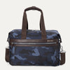 A camouflage-patterned underseat tote bag with full-grain leather details and a Travelpro logo, featuring a brown leather handle and shoulder strap, and a front zipper pocket.
