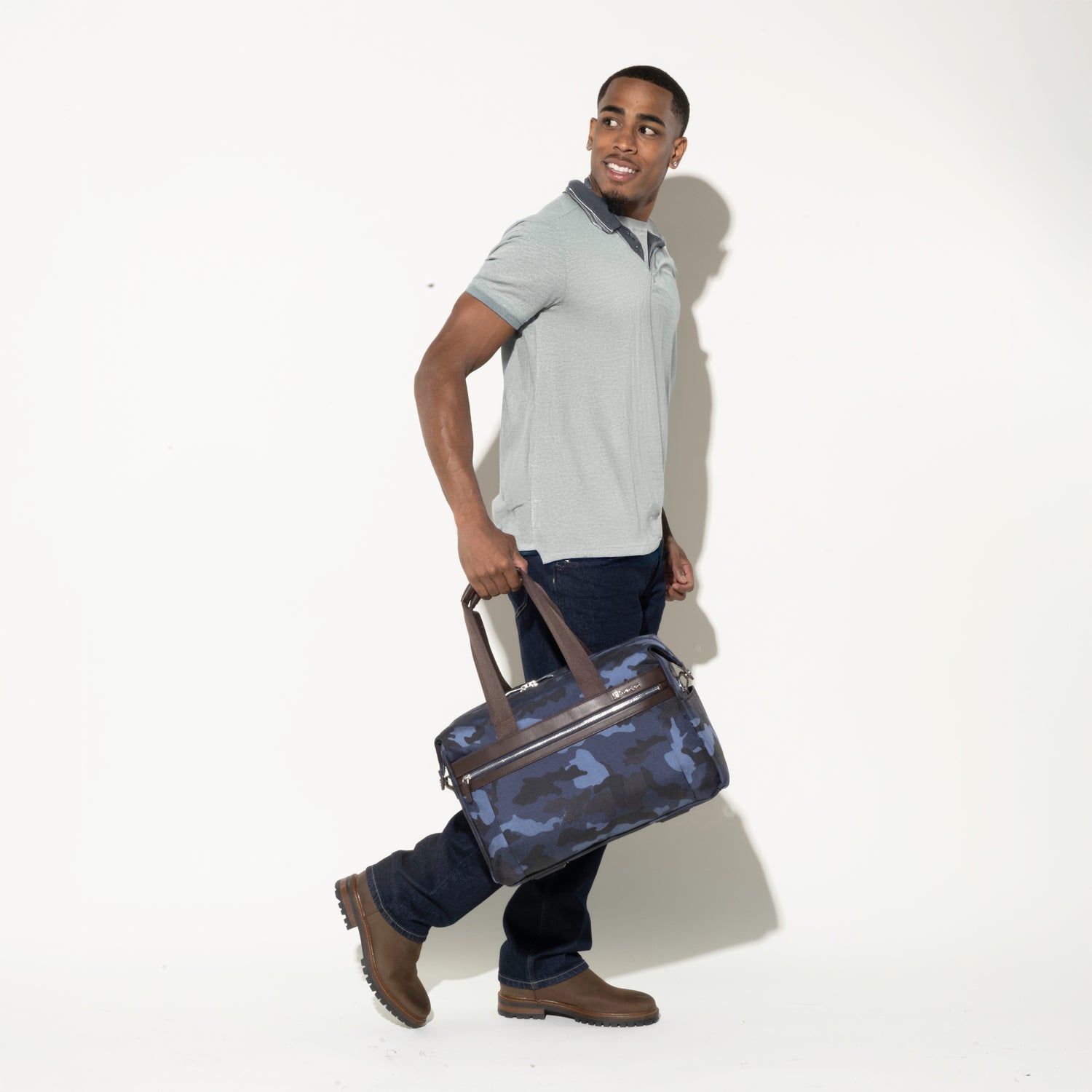 Man walking while carrying the Platinum® Elite Soft Duffel in Camouflage, featuring dual top handles and a zippered front pocket