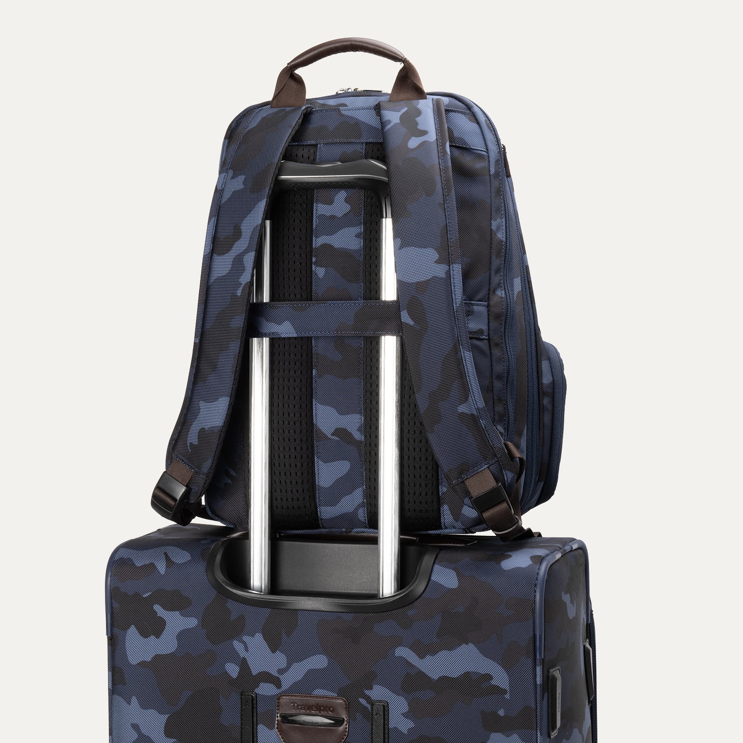 **Alt text:** Rear view of the Platinum® Elite Business Backpack in blue camouflage, secured to a matching suitcase handle using its built-in luggage pass-through strap.
