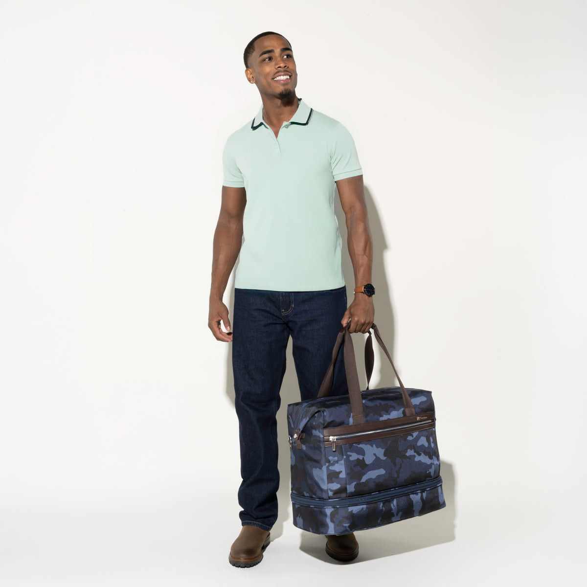 Man standing and smiling while holding the Platinum® Elite Drop-Bottom Weekender in Camouflage, featuring dual top carry handles and a zippered drop-bottom compartment