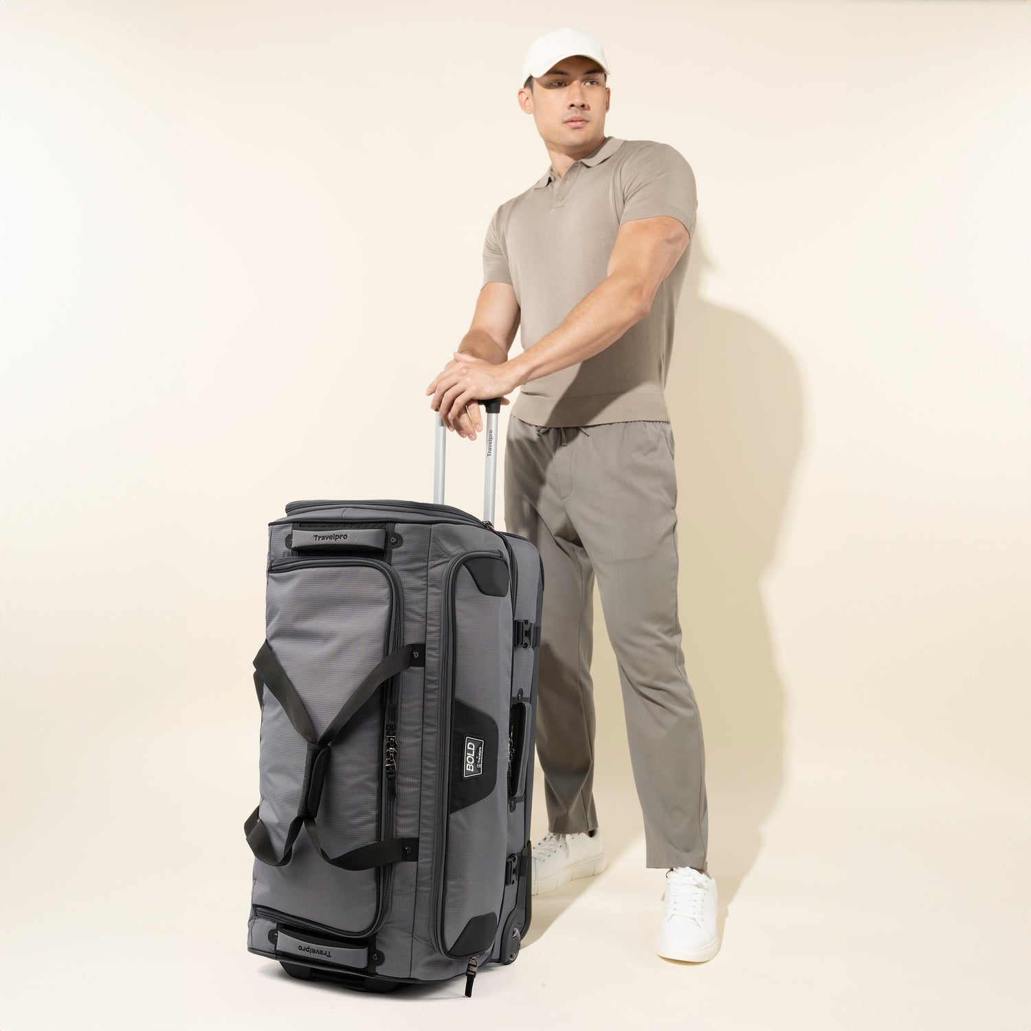 Man holding the extension handle of a Bold™ by Travelpro® Drop-Bottom Expandable Rolling Duffel in Grey/Black.