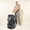 Man holding the extension handle of a Bold™ by Travelpro® Drop-Bottom Expandable Rolling Duffel in Grey/Black.