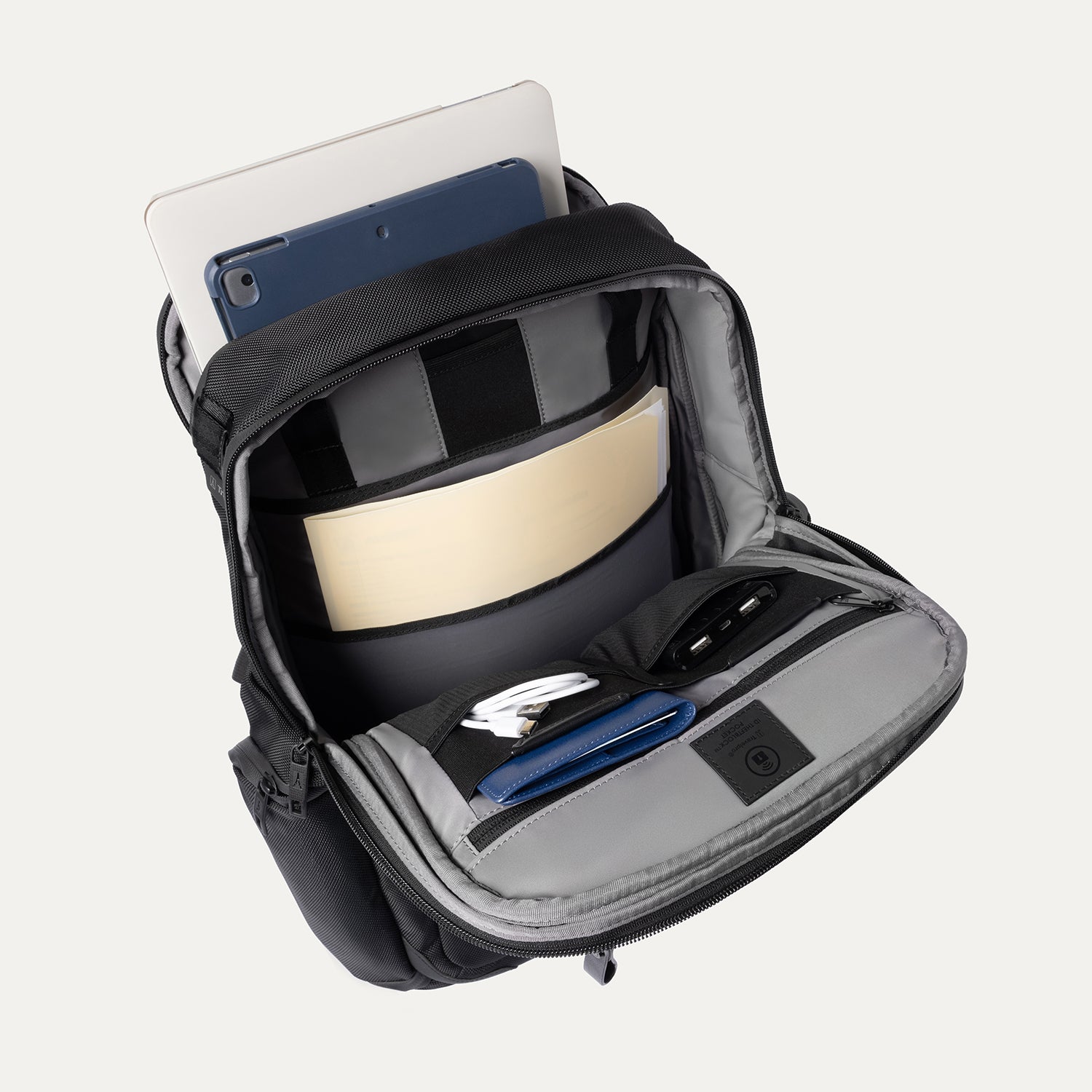 Black backpack with compartments containing a tablet, notebook, and other items on a white background