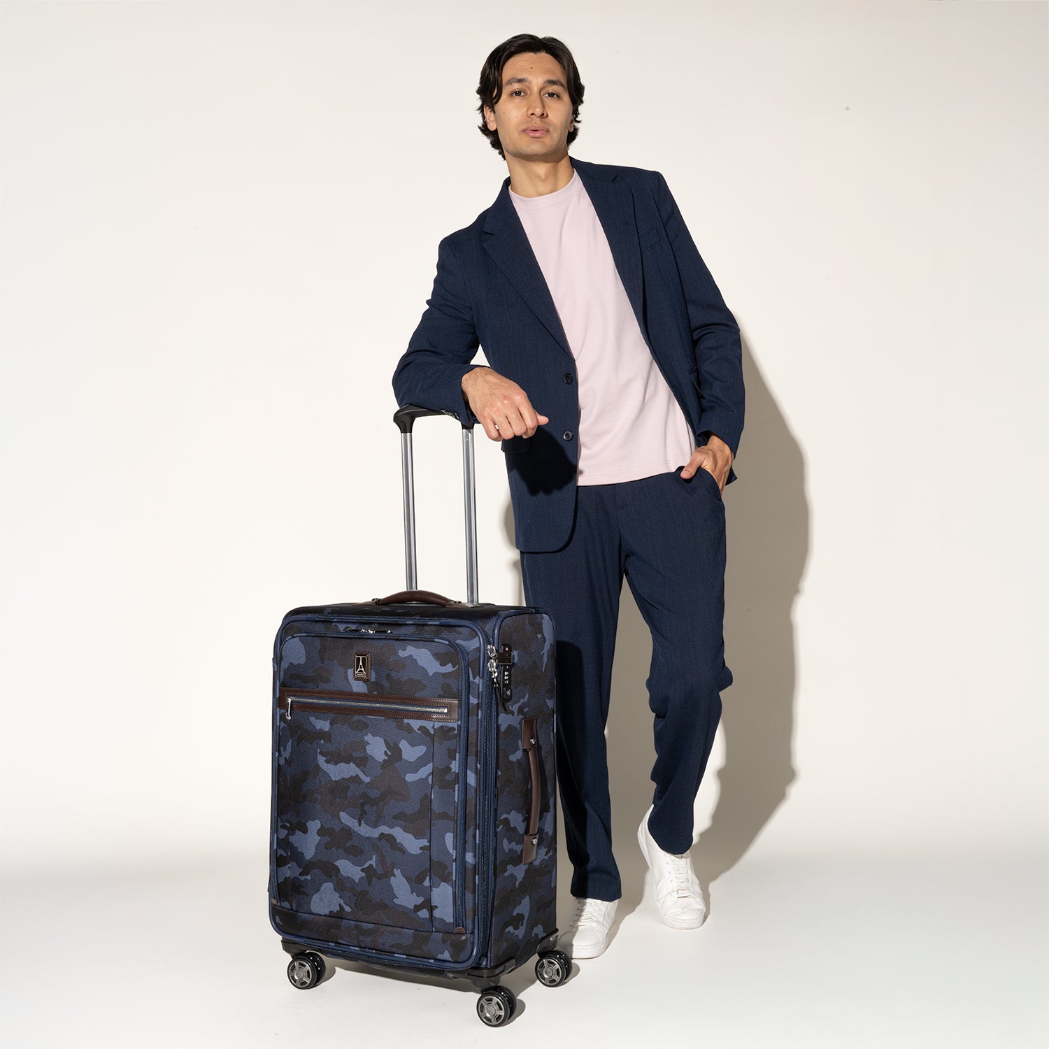 Person standing beside the Travelpro Platinum Elite Medium Check-In Spinner in Camouflage, gripping the extended handle.