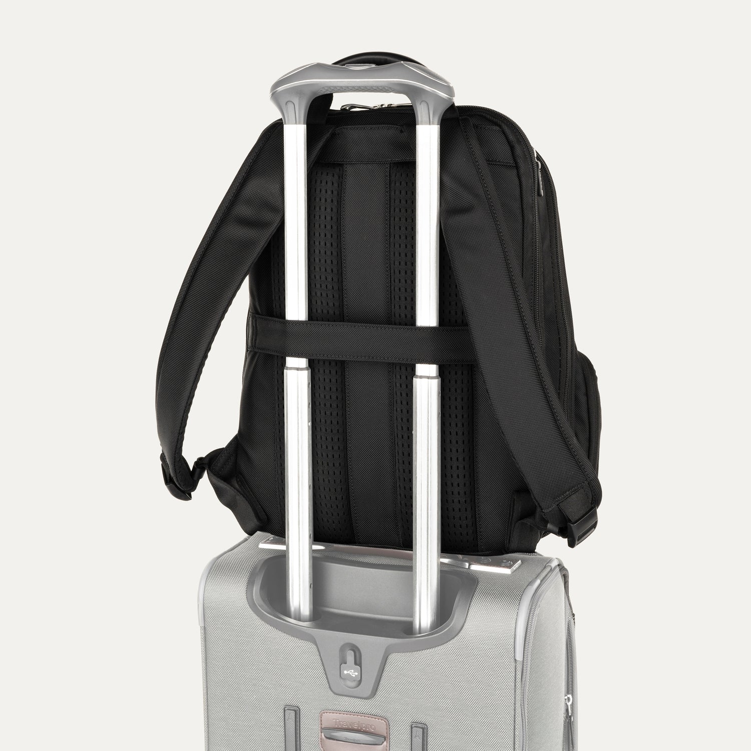 Black backpack with a rear strap over suitcase handle on a white background