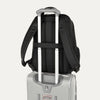 Black backpack with a rear strap over suitcase handle on a white background