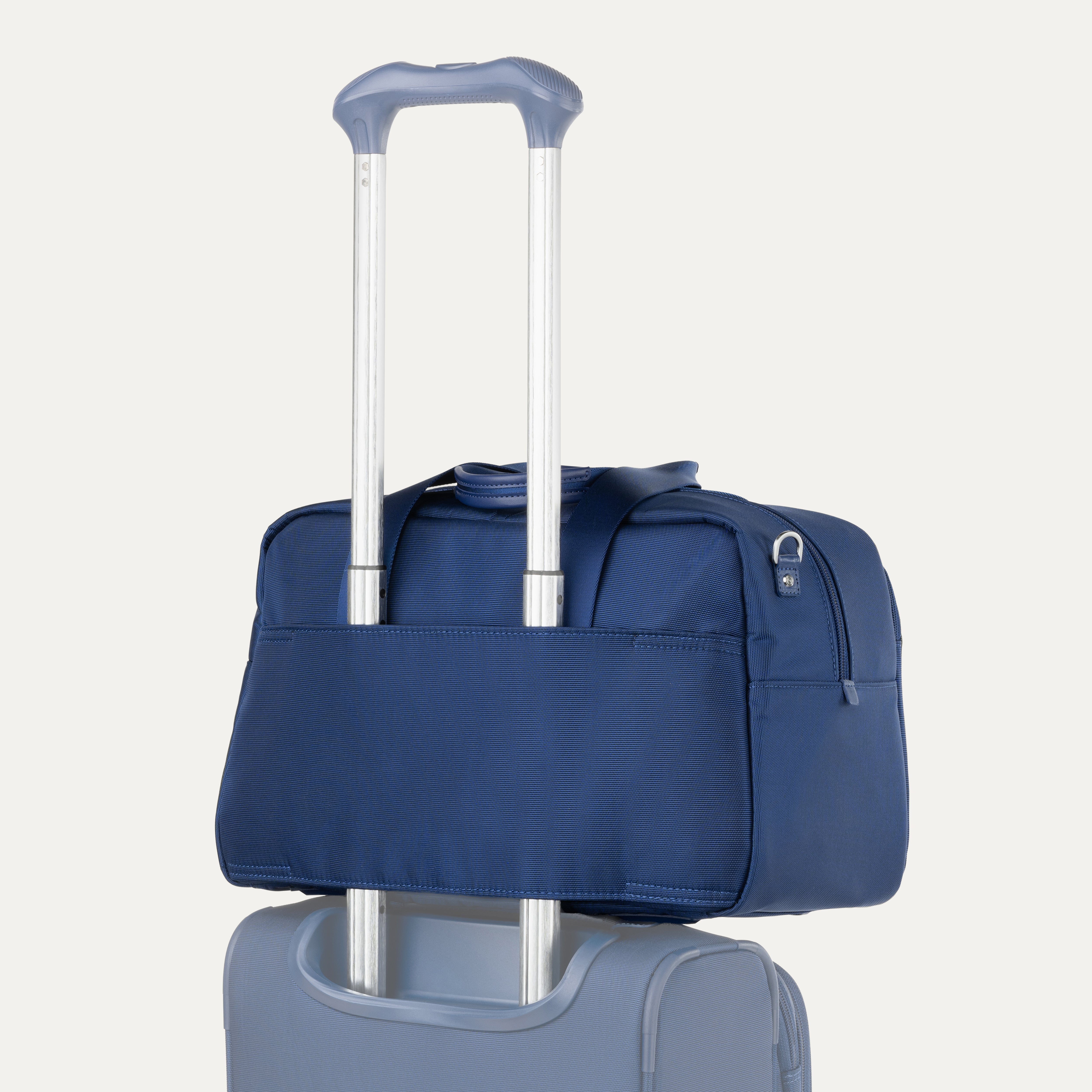 Blue tote bag with a silver handle on top of a suitcase against a white background
