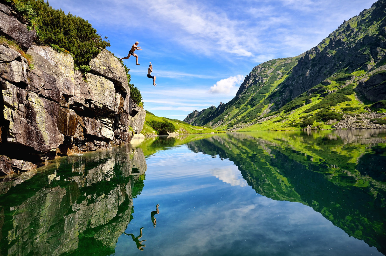 2 people jumping off a cliff into a lake