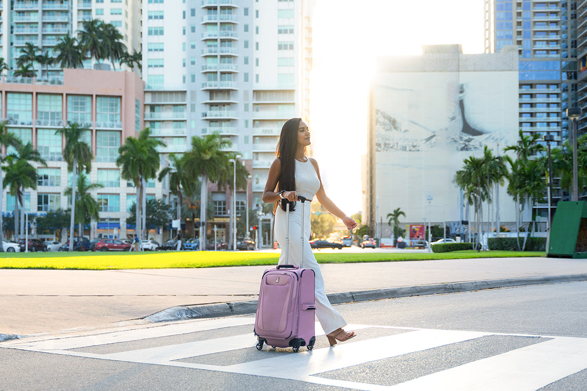 Woman rolling a pink suitcase along a palm-lined street in Miami, Florida.