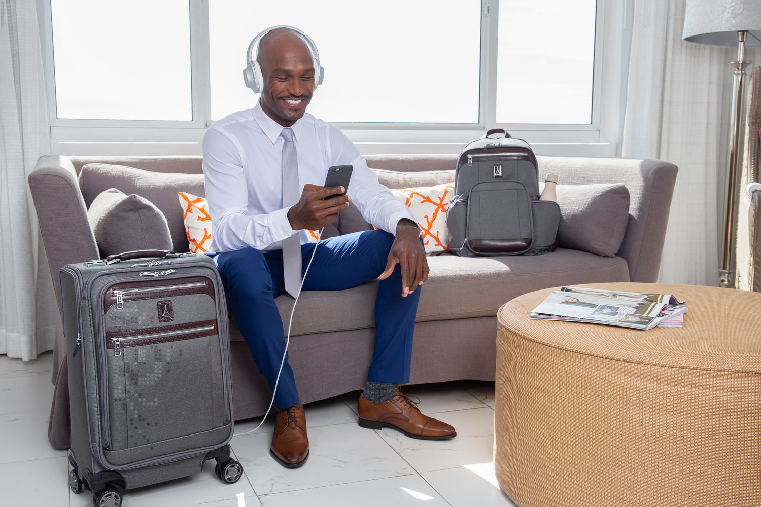 business man listening to music and looking at his phone. Sitting in a hotel room with soft side luggage