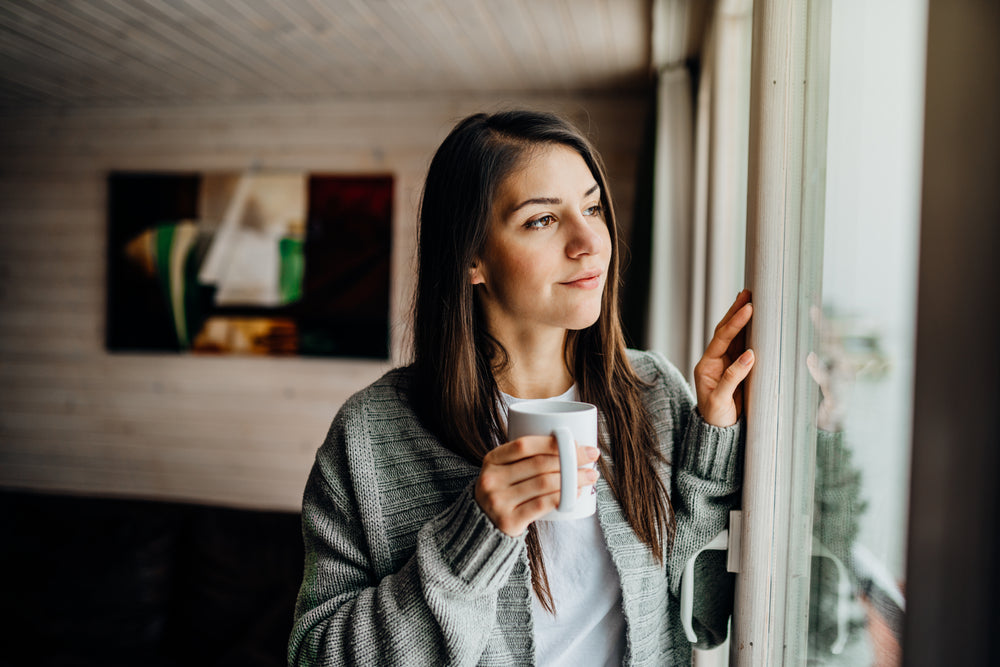 woman looking outside with a cup of coffee in her hand