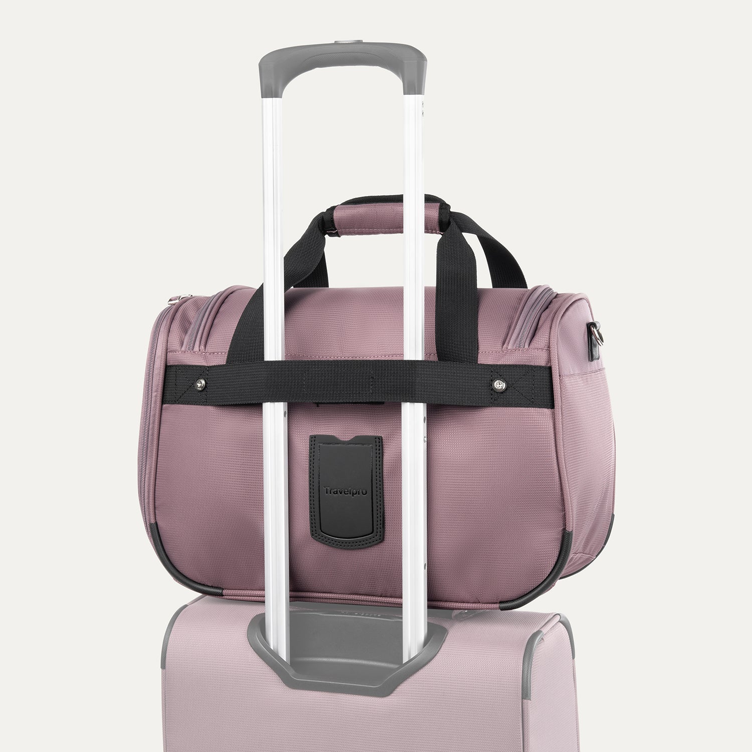 rear view of the dusty rose pink travelpro maxlite 5 soft tote stacked on a suitcase handle using the integrated rear attachment strap for hands-free mobility.