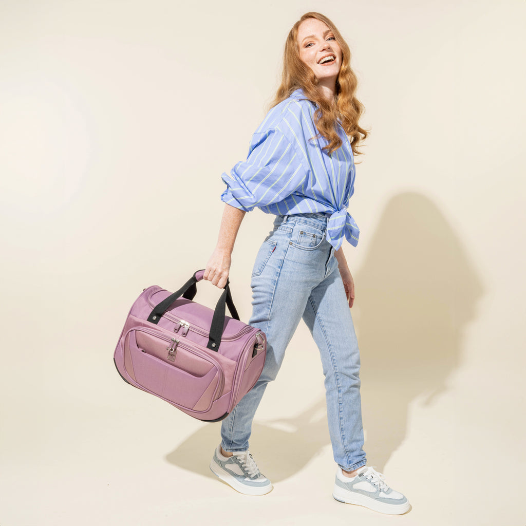 lifestyle view of a woman carrying the dusty rose pink travelpro maxlite 5 soft tote by its top carry handles while walking, showcasing the bag's compact size and portable design.