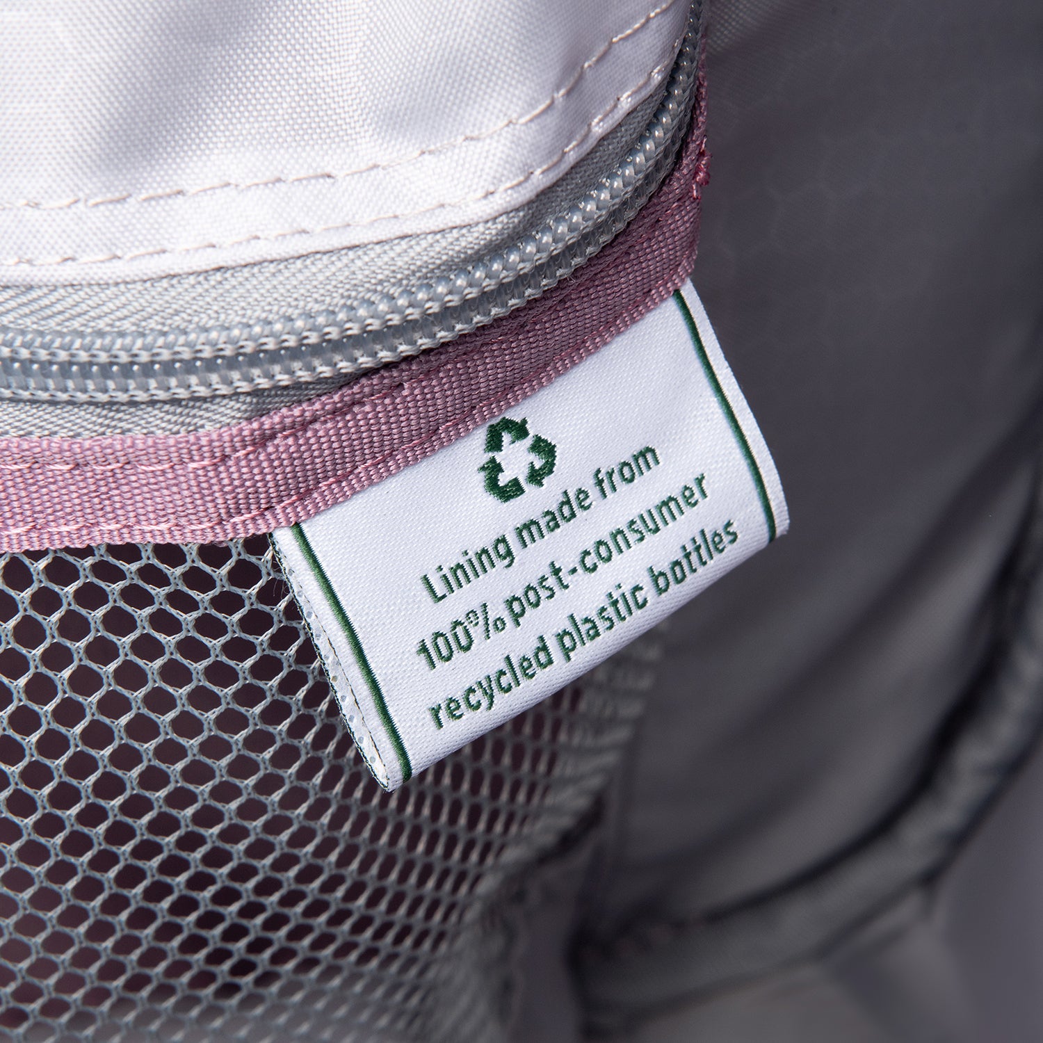 close up of the interior fabric tag on the dusty rose pink travelpro maxlite 5 soft tote showing a green recycling symbol and text stating lining made from 100 percent post consumer recycled plastic bottles.