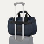 Blue tote with a black rear strap over suitcase handle on a white background