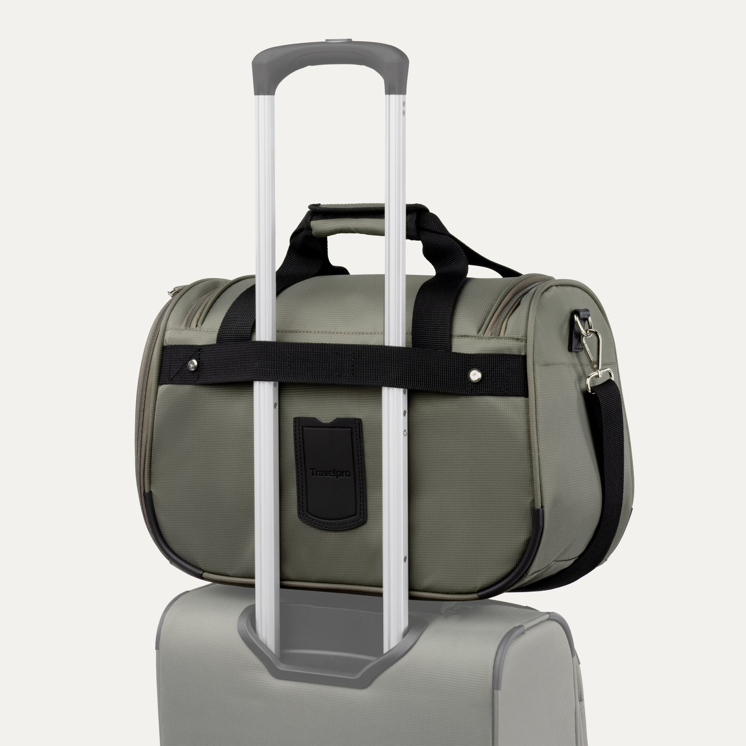 green tote with a black rear strap over suitcase handle on a white background