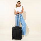 Woman standing with a Travelpro® Maxlite® 5 International Carry-On Rollaboard® in black, hand resting on the extended handle.