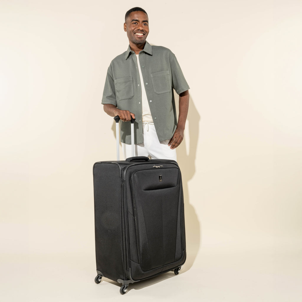 lifestyle view of a man standing behind the black travelpro maxlite 5 large check-in spinner showing the suitcase's tall profile and extended powerscope lite handle.