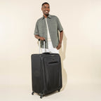 lifestyle view of a man standing behind the black travelpro maxlite 5 large check-in spinner showing the suitcase's tall profile and extended powerscope lite handle.