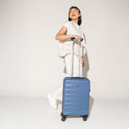 Person walking with the Travelpro Maxlite Air Carry-On Hardside Spinner in Ensign Blue, highlighting lightweight maneuverability.
