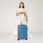 Person standing with the Travelpro Maxlite Air Carry-On Hardside Spinner in Teal, showcasing balanced upright handling.
