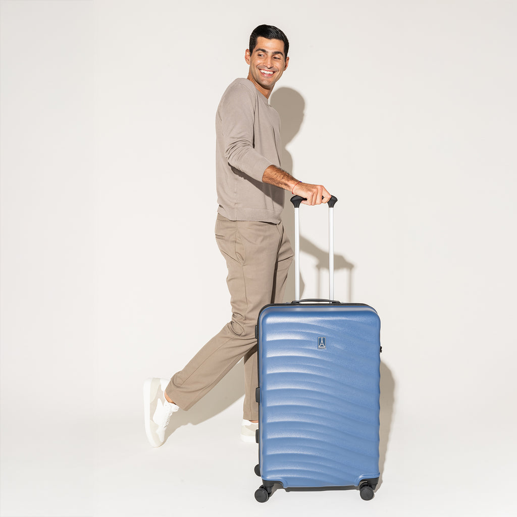 Person walking with the Travelpro Maxlite Air Medium Check-In Hardside Spinner in Ensign Blue, featuring 360° spinner wheels.
