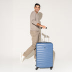 Person walking with the Travelpro Maxlite Air Medium Check-In Hardside Spinner in Ensign Blue, featuring 360° spinner wheels.