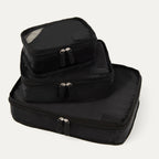A set of three black Travelpro packing cubes, with the largest at the bottom, medium in the middle, and the smallest at the top, all with zipper closures.