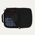 Travelpro® Medium Packing Cube in black, shown partially unzipped with clothes neatly packed inside.
