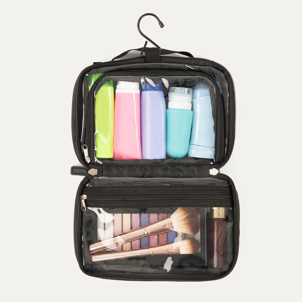 A toiletry bag open and organized with various grooming and cosmetic items visible through clear windowed compartments, featuring a hanger hook, and a black webbing handle.