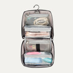 A hanging toiletry organizer with clear zippered compartments, containing various toiletry items like bottles and a brush. The organizer is open and hanging against a plain background.