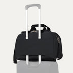 Travelpro® Essentials™ 2-in-1 Travel Tote & Cooler in Black, shown securely attached to a rolling suitcase handle using its rear strap, demonstrating its convenient stacking ability