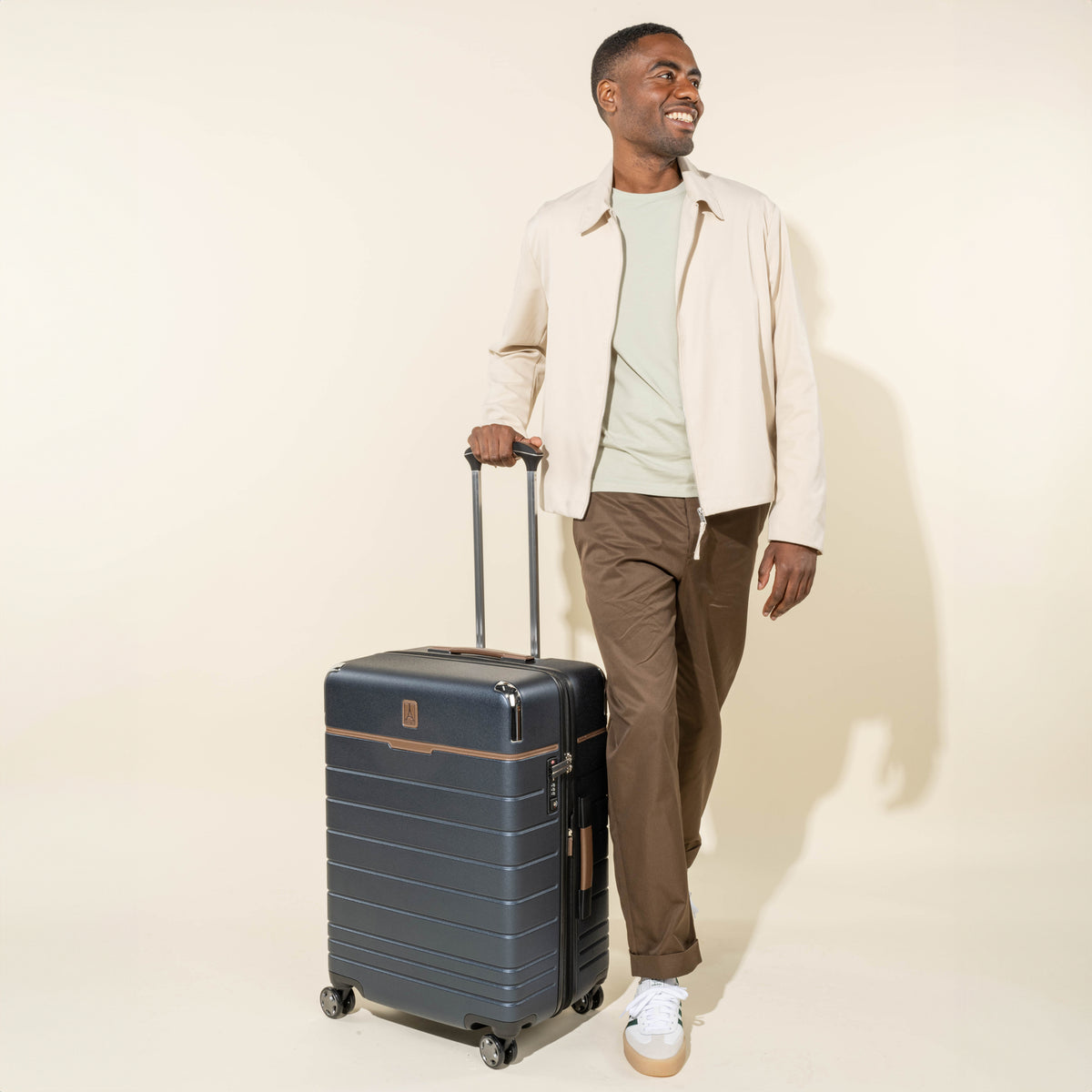 Man holding the telescoping handle of a Travelpro® x Travel + Leisure® Medium Check-In Spinner in Monaco Blue.

