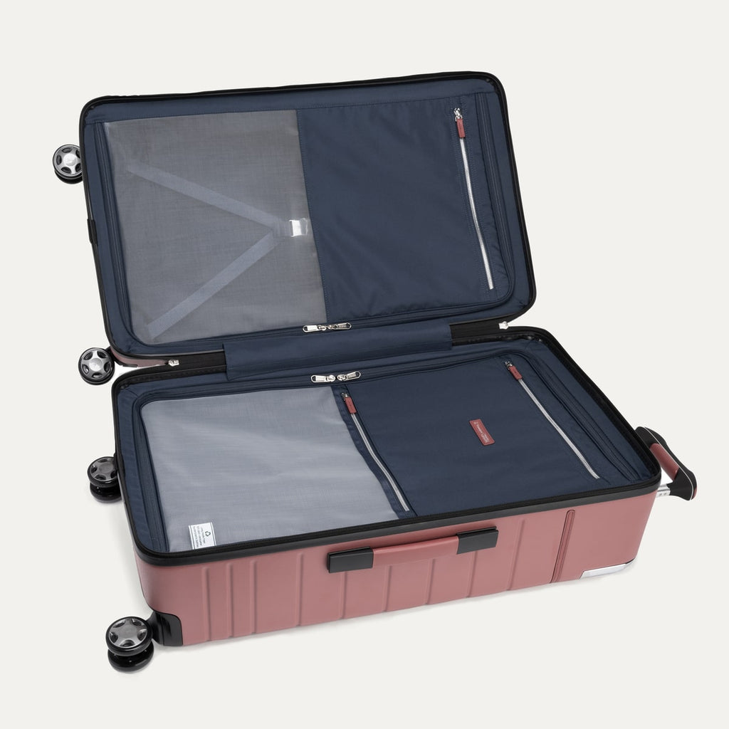 interior view of the open astro dust red travelpro x travel plus leisure large check-in trunk spinner, featuring a spacious split-case design with fully lined navy blue fabric, zippered privacy separator panels with mesh detailing, and premium silver metal zipper pulls.