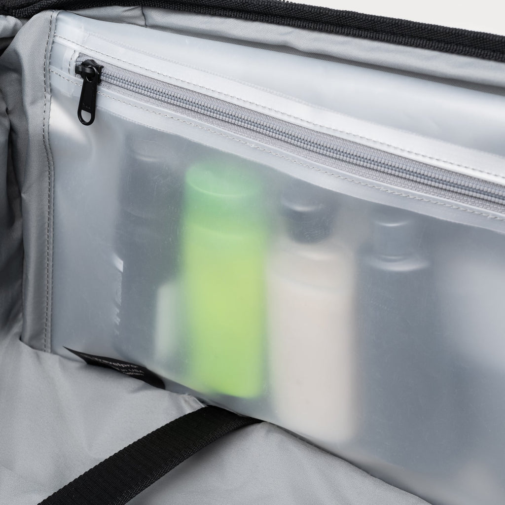 Clear interior view of suitcase with translucent zippered pouch holding upright travel-size toiletry bottles.

