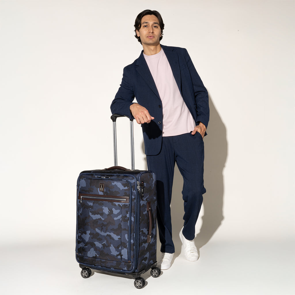 Person standing beside the Travelpro Platinum Elite Medium Check-In Spinner in Camouflage, gripping the extended handle.
