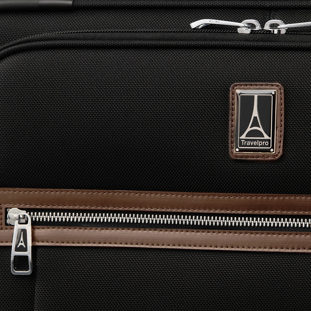 Close-up of the Travelpro logo patch, leather-trimmed front pocket, and chrome zipper accents on the Platinum® Elite Medium Check-In Spinner - Limited Edition Colors in Heritage Black.