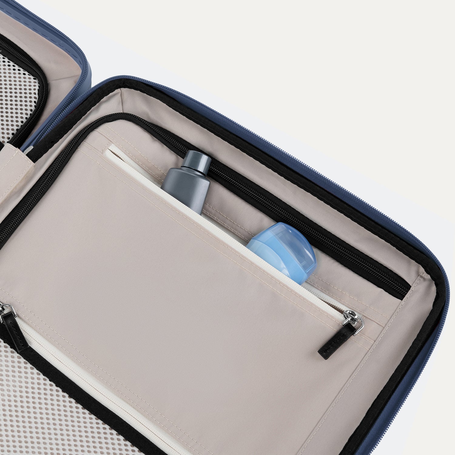 Interior view of Travelpro Platinum Elite Compact Carry-On Hardside Spinner in Dark Sky Blue, showing zippered pocket with visible travel-size toiletries.
