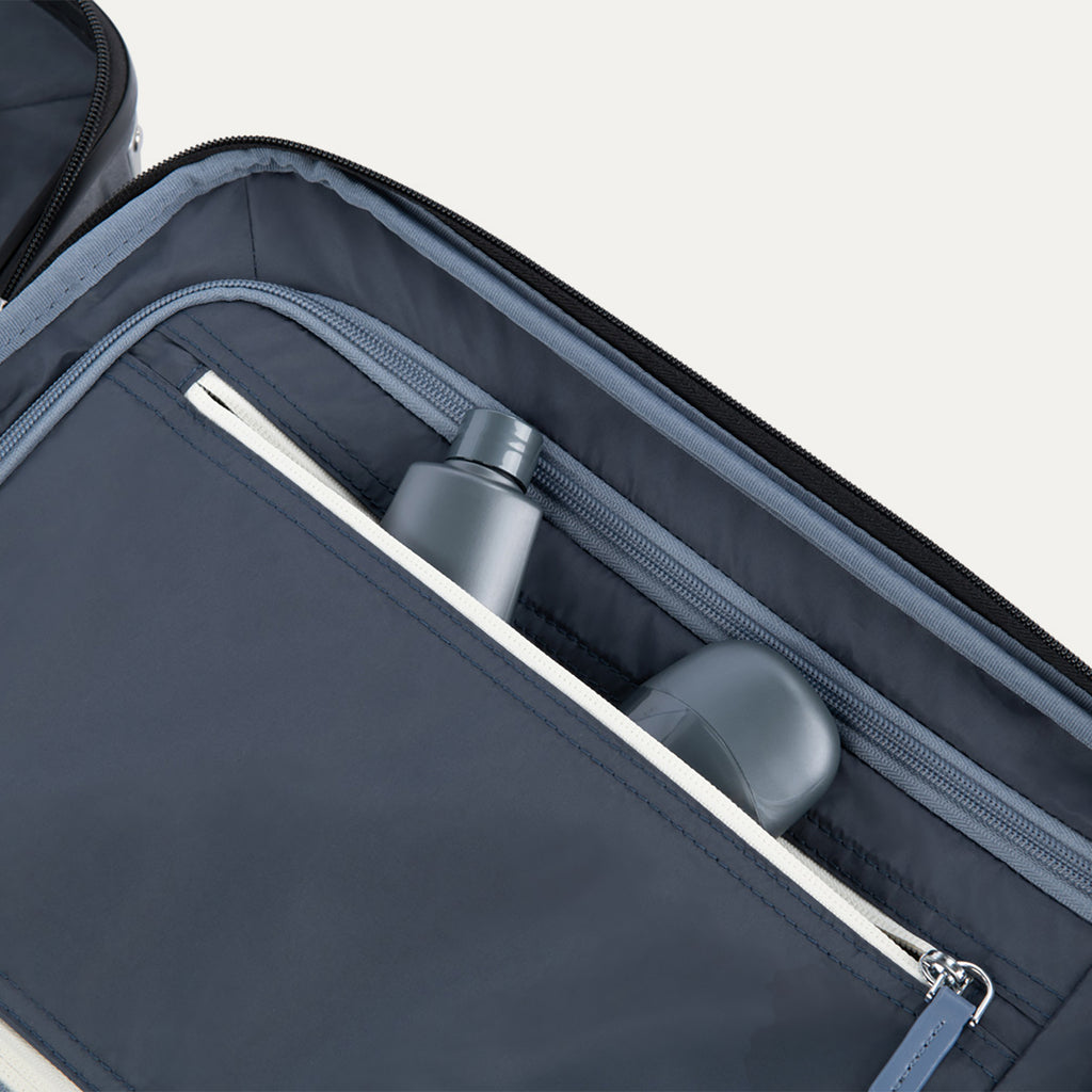 Interior view of Travelpro Platinum Elite Compact Carry-On Hardside Spinner in Shadow Black, showing zippered pocket with visible travel-size toiletries.
